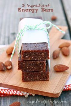 three pieces of brownie sitting on top of a wooden cutting board next to nuts