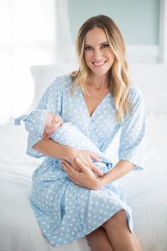 a woman sitting on top of a bed holding a baby wrapped in a blue polka dot blanket