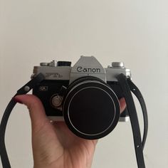 a person holding up a camera in front of a white wall with the words canon on it