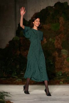 a woman in a green dress waves to the crowd as she walks down a runway