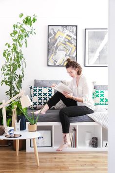 a woman sitting on a couch reading a book next to a potted plant in a living room