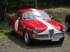 an old red and white car parked on gravel