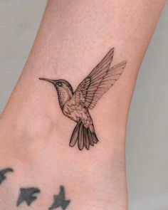 a small hummingbird tattoo on the ankle with stars in the back ground and an arrow behind it