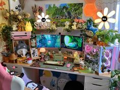 a desk with two computer monitors on top of it next to plants and stuffed animals