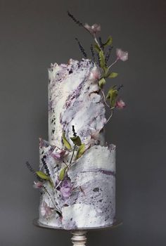 a three tiered cake with flowers on top is decorated in white and purple marble