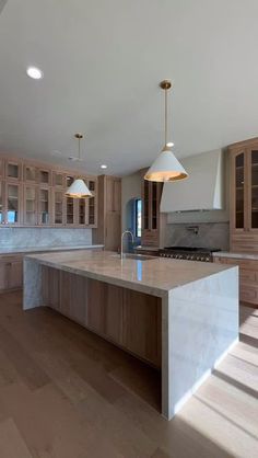 a large kitchen with wooden cabinets and marble counter tops, two pendant lights over the island