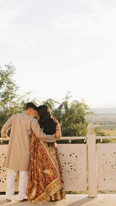 a man and woman standing next to each other on top of a white fence with trees in the background