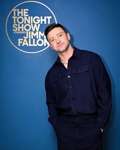 a man standing in front of a blue wall with the tonight show logo on it