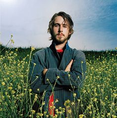 a man standing in the middle of a field with his arms crossed and looking at the camera