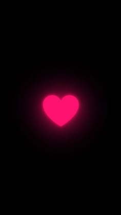 a pink heart is glowing in the dark