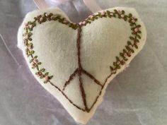 a white heart shaped decoration hanging from a ribbon on a piece of cloth with pink and green flowers