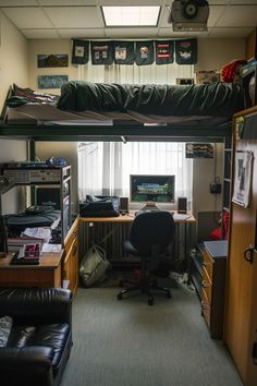 A small, organized dorm room with a loft bed, desk setup with a computer, books, and decorations. Dark Aesthetic Dorm Room Ideas, Dorm Room Ideas Dark, Room Ideas Dark Aesthetic, Goth College Dorm, College Dorm Room Ideas Goth, Dorm Room Designs For Guys, Dorm Room Goth, Aesthetic Men’s Dorm Room, College Dorm Room Ideas For Guys