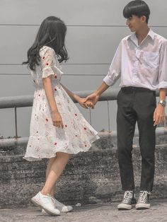 a young man and woman holding hands while standing next to each other on a bridge