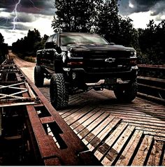 a black truck driving down a road under a cloudy sky with lightning in the background