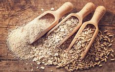 two wooden scoops filled with oats next to a pile of oatmeal