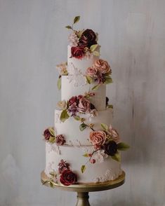 a three tiered cake with flowers and leaves on the top is sitting on a gold pedestal