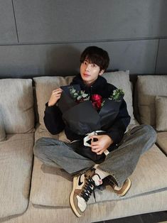 a young man sitting on top of a couch holding a black paper bag and flowers