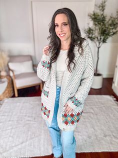 a woman standing in front of a white rug wearing jeans and a cardigan sweater