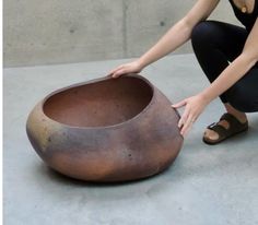 a woman kneeling down next to a large pot on the ground with her hands in it