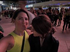 two women standing next to each other in front of a group of people at an airport