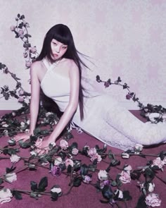 a woman sitting on the ground surrounded by flowers and vines, with her hair blowing in the wind