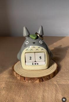 a ceramic clock that is shaped like a totoro sitting on top of a tree stump