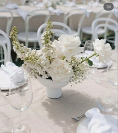 white flowers in a vase on top of a table with wine glasses and napkins