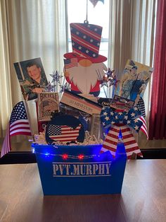 a gift box with patriotic items in it on a wooden table next to a window