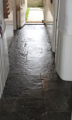 an open door leading into a hallway with stone flooring and white trim on the walls