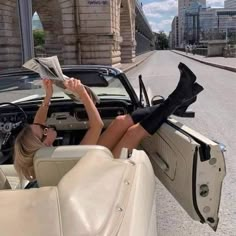 a woman sitting in the driver's seat of a convertible car reading a magazine