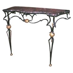 an ornate console table with marble top and metal legs, decorated with gold orbs