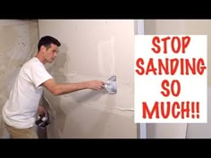 a man is painting the wall with a sprayer and a sign that says stop sanding so much