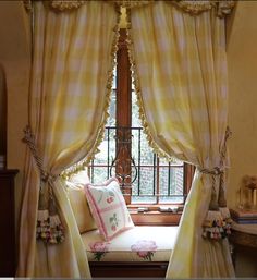 a window seat in front of a window with curtains and pillows on top of it