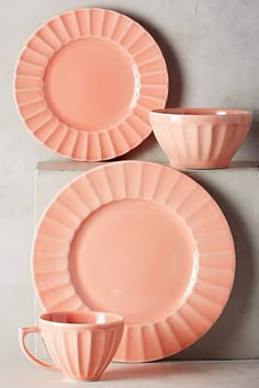 pink plates and cups sitting on top of each other in front of a gray wall