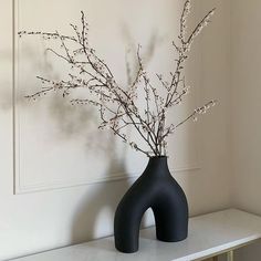 a black vase with white flowers in it on a shelf next to a wall mounted art piece