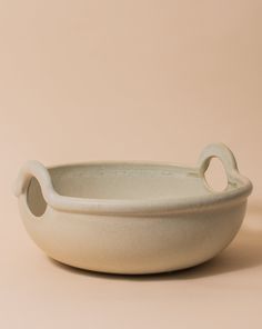 a white bowl sitting on top of a table next to a brown wall with an oval handle