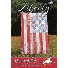 an american flag quilt hanging on the side of a field with trees in the background