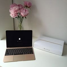 an open laptop computer sitting on top of a white desk next to a vase with pink flowers