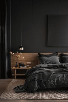 a bed with black sheets and pillows in a dark room next to a painting on the wall