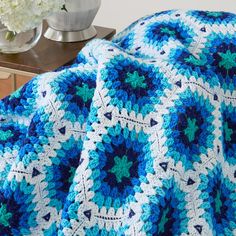 a blue and white crocheted afghan on a table next to a vase with flowers