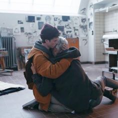 a man sitting on the floor holding a dog in his lap and hugging it's face