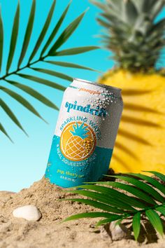 a can of spinach sparkling in the sand next to a pineapple