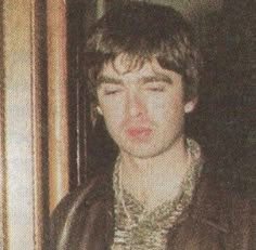 the young man is wearing a leather jacket and has his eyes closed while standing in front of a door