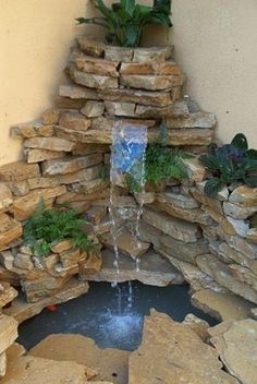 a water fountain in the corner of a building with rocks and plants growing out of it