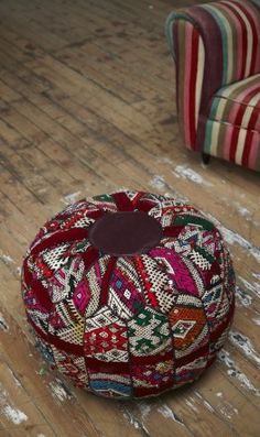 a red ottoman sitting on top of a wooden floor next to a striped couch and chair