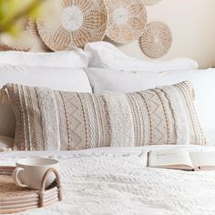 a white bed topped with lots of pillows next to a basket filled with books and cups