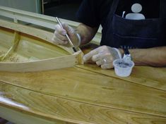 a man working on a wooden boat in a woodworking shop with a paintbrush