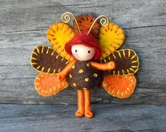 a small doll with a red hat and orange wings on it's head is standing in front of a wooden plank