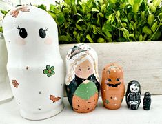 three wooden dolls sitting next to each other in front of some potted plants and bushes