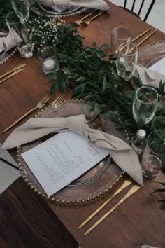 the table is set with silverware and greenery